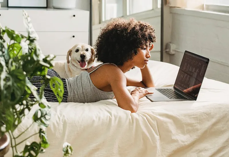 Lying woman on bed with dog and laptop