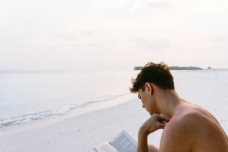 Mann liest Buch am Strand